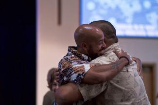 Two African American / Latino men smiling and hugging tightly.