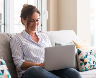 Middle aged woman using laptop in the sofa with a happy face.